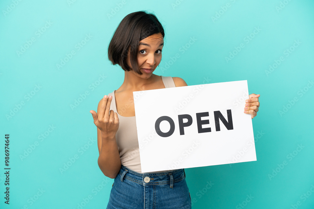 Young mixed race woman isolated on blue background holding a placard with text OPEN and doing coming gesture Young mixed race woman isolated on blue background holding a placard with text OPEN and doing coming gesture