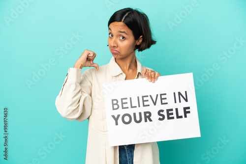 Young mixed race woman isolated on blue background holding a placard with text Believe In Your Self with proud gesture