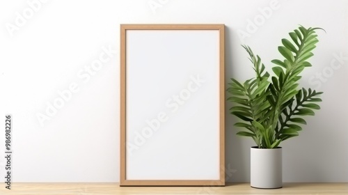 A wooden frame with a blank canvas sits on a wooden tabletop, beside a potted green plant.