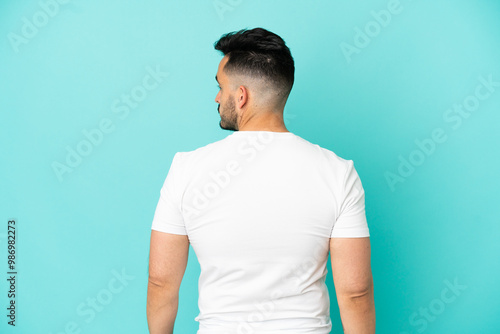 Young caucasian man isolated on blue background in back position and looking side