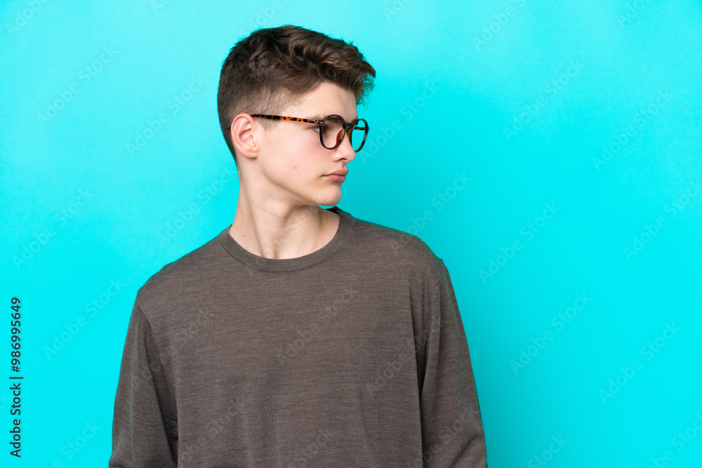 Teenager Russian man isolated on blue background looking side Teenager Russian man isolated on blue background looking side