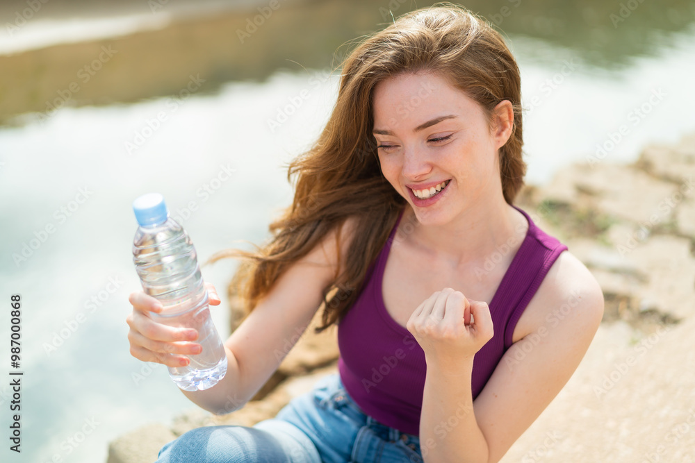 Young redhead woman with a bottle of water at outdoors celebrating a victory Young redhead woman with a bottle of water at outdoors celebrating a victory