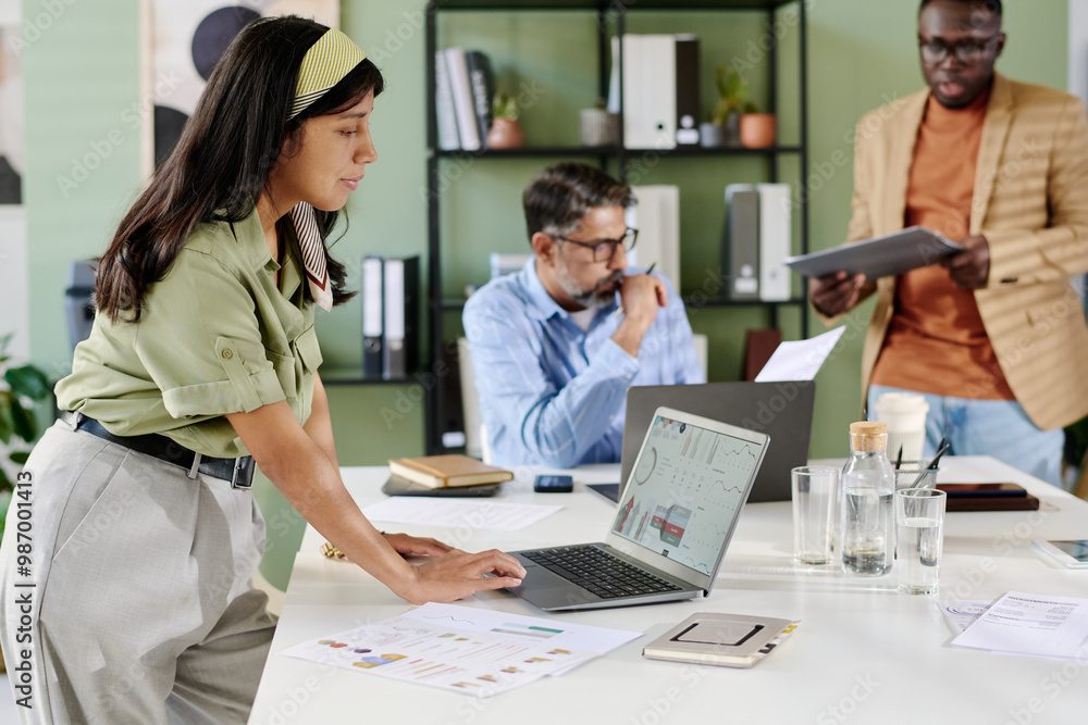Obraz premium Team of professionals engaged in design project, with emphasis on teamwork and diverse skill sets collaborating at modern workplace. Laptop, documents, and gadgets are central to operation
