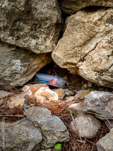 A common geocache plastic container hidden between rocks of a rural stone wall of Mallorca offers a typical geocaching experience, merging recreation and nature, appealing to geocaching enthusiasts.