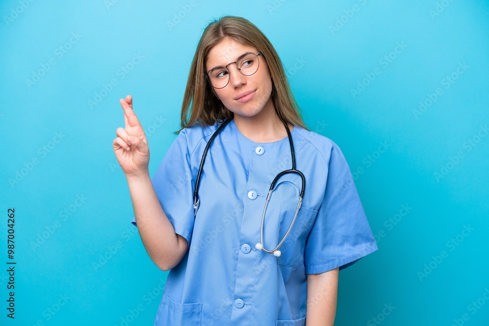 Young surgeon doctor woman isolated on blue background with fingers crossing and wishing the best Young surgeon doctor woman isolated on blue background with fingers crossing and wishing the best