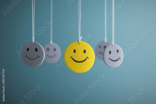 Emotions. Gray and happy yellow smileys hanging on threads. Blue background. State of mind photo