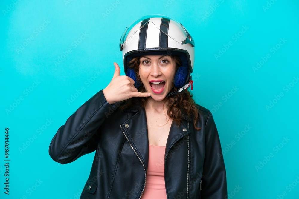 Young caucasian woman with a motorcycle helmet isolated on blue background making phone gesture. Call me back sign Young caucasian woman with a motorcycle helmet isolated on blue background making phone gesture. Call me back sign