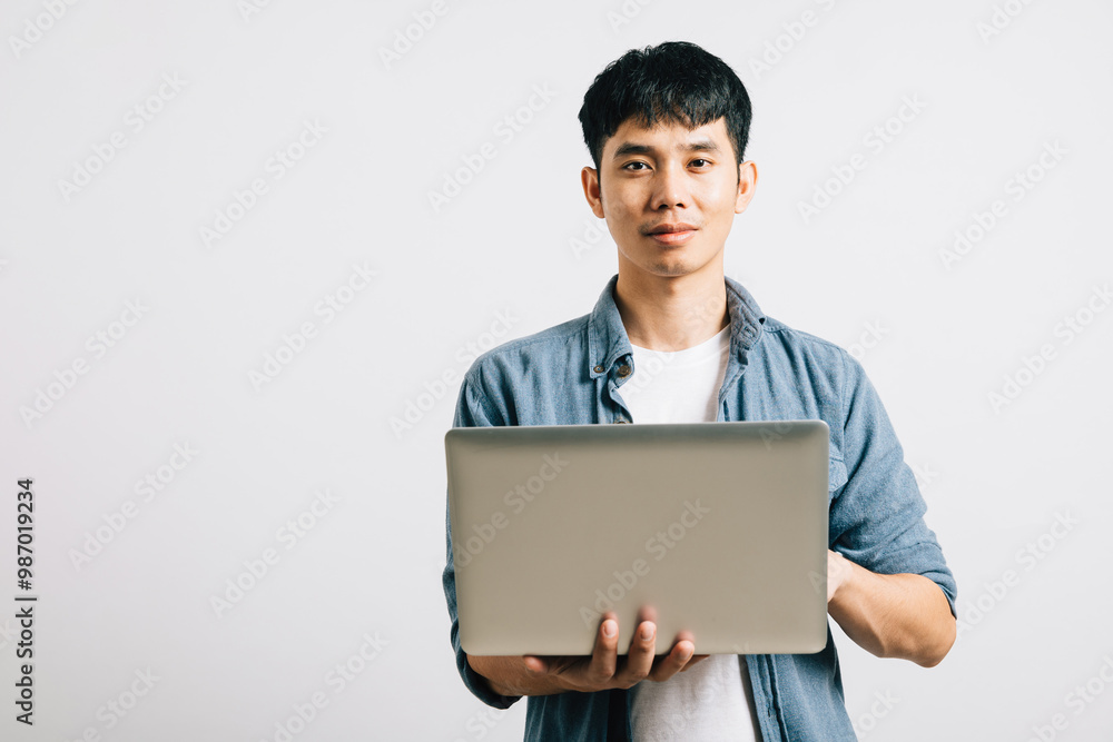 Confident and excited, a young Asian man smiles while working on a laptop, sending emails or chatting online. Studio shot isolated on white background, emphasizing his technological prowess. Confident and excited, a young Asian man smiles while working on a laptop, sending emails or chatting online. Studio shot isolated on white background, emphasizing his technological prowess.