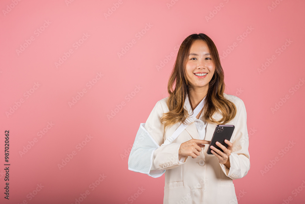 Woman confident smiling broken arm after accident and wear arm splint for treatment and hold smartphone, happy Asian female sling supported hand isolated on pink background, social media, copy space Woman confident smiling broken arm after accident and wear arm splint for treatment and hold smartphone, happy Asian female sling supported hand isolated on pink background, social media, copy space