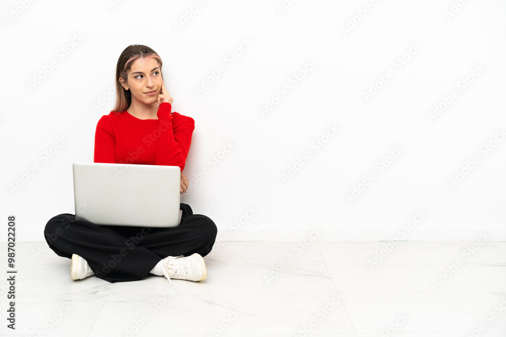 Young caucasian woman with a laptop sitting on the floor thinking an idea while looking up Young caucasian woman with a laptop sitting on the floor thinking an idea while looking up