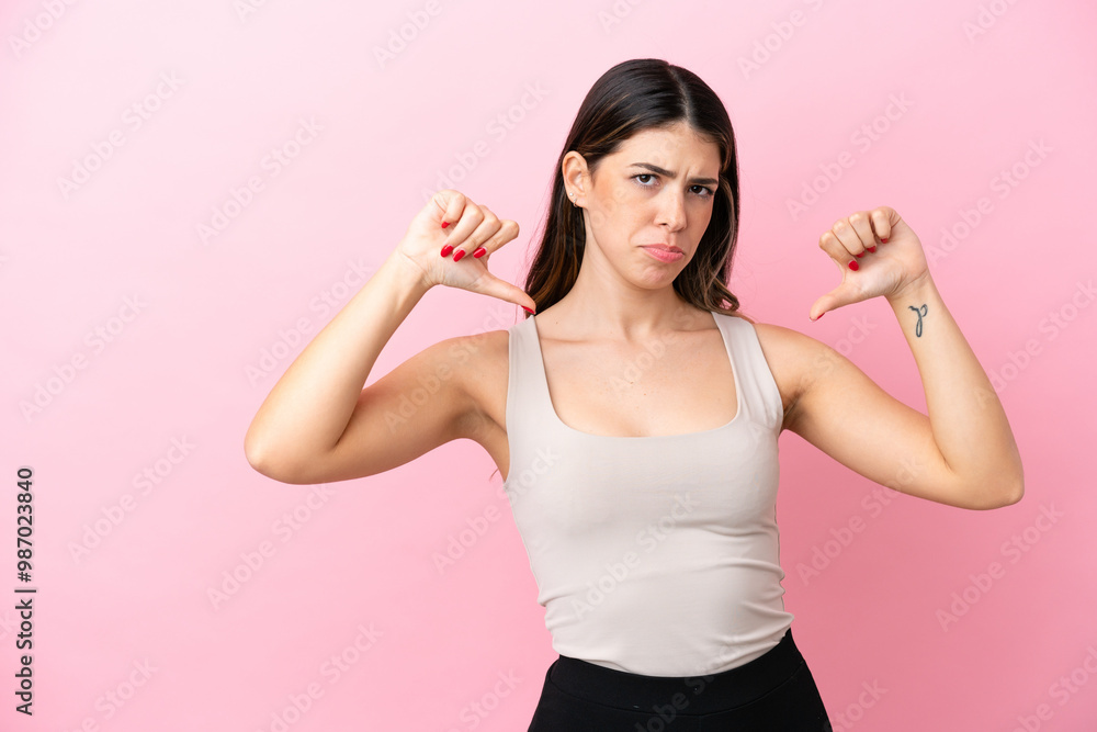 Young Italian woman isolated on pink background showing thumb down with two hands Young Italian woman isolated on pink background showing thumb down with two hands