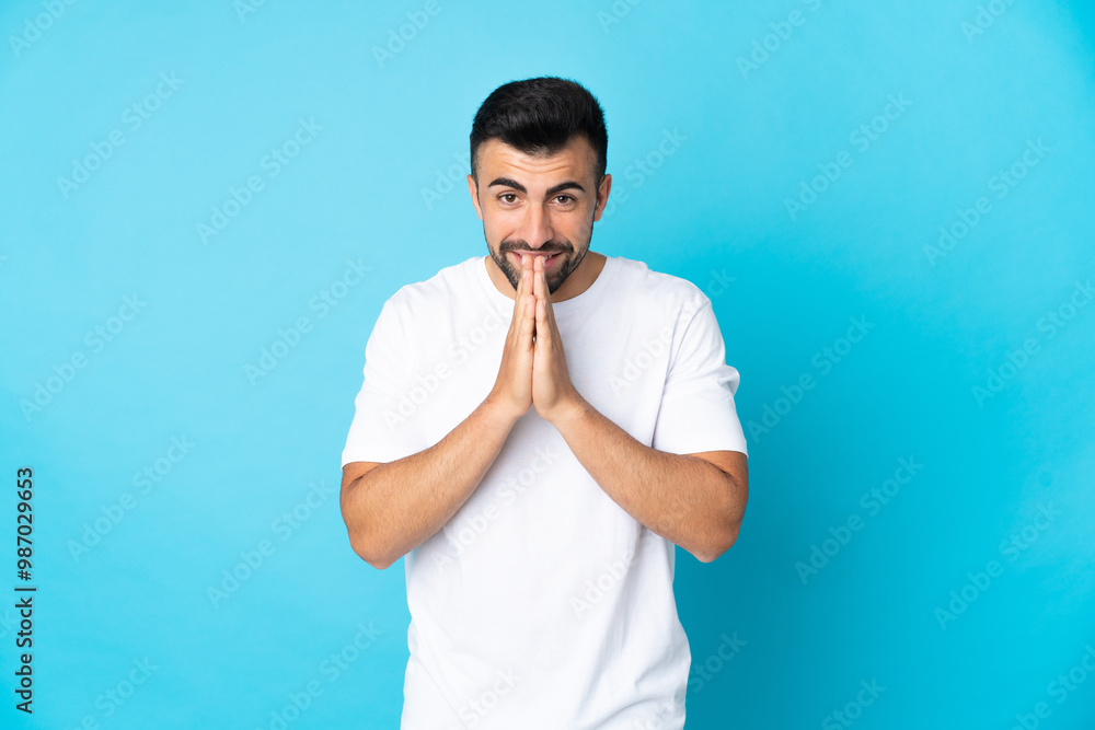 Caucasian man over isolated blue background keeps palm together. Person asks for something Caucasian man over isolated blue background keeps palm together. Person asks for something