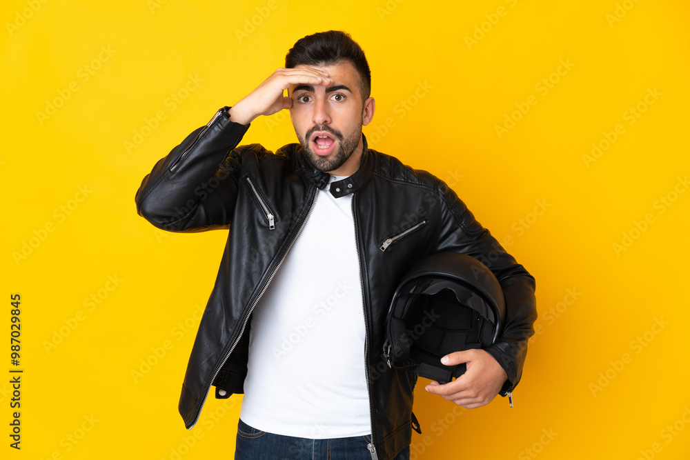 Caucasian man with a motorcycle helmet over isolated yellow background doing surprise gesture while looking to the side Caucasian man with a motorcycle helmet over isolated yellow background doing surprise gesture while looking to the side