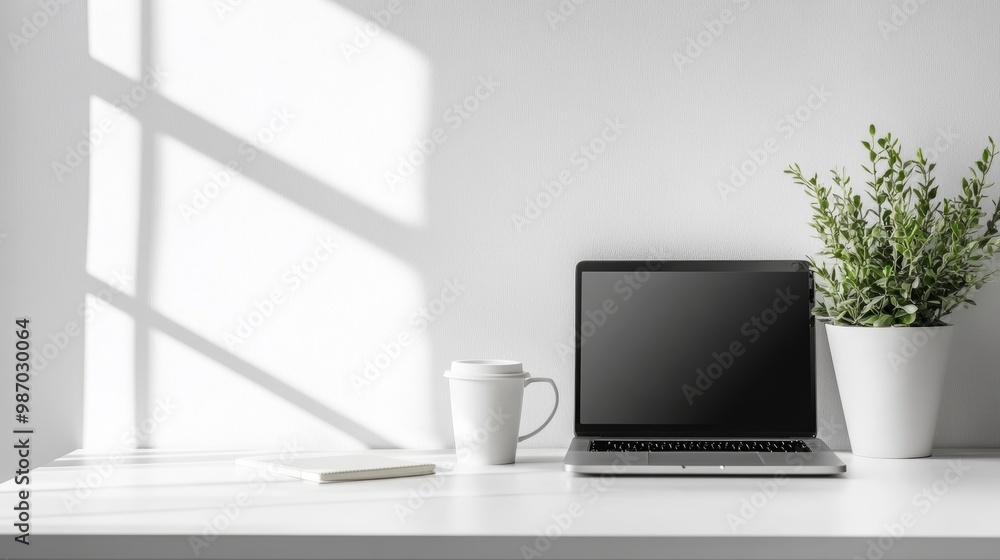 Fototapeta premium A modern, minimalist workspace featuring a laptop, coffee cup, and plant on a white desk.