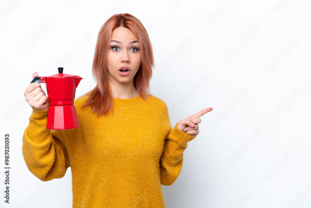 Young Russian girl holding coffee pot isolated on white background surprised and pointing finger to the side Young Russian girl holding coffee pot isolated on white background surprised and pointing finger to the side
