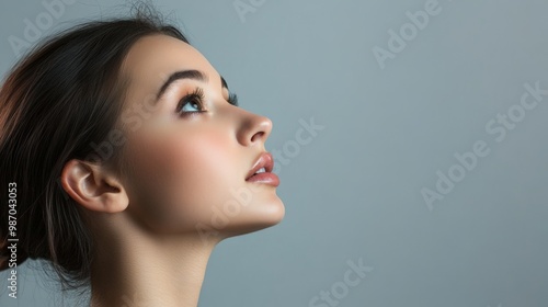 Close-up portrait of young woman gazing upward against grey background