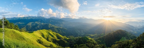  The sun brightly shines through clouds, illuminating a mountain range Green grass and mountains comprise the foreground