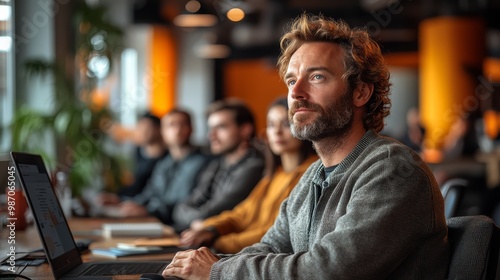 Professional training session with attentive participants in a modern office. Focused man at laptop, blurred colleagues in background.