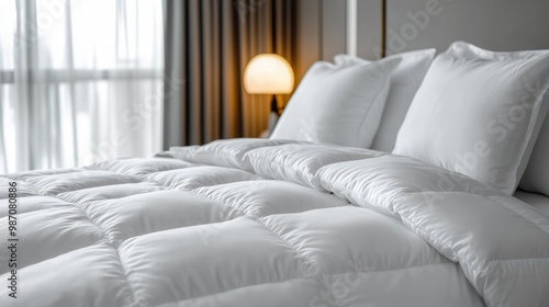 A white, fluffy down duvet and two white pillows on a bed in a hotel room. photo