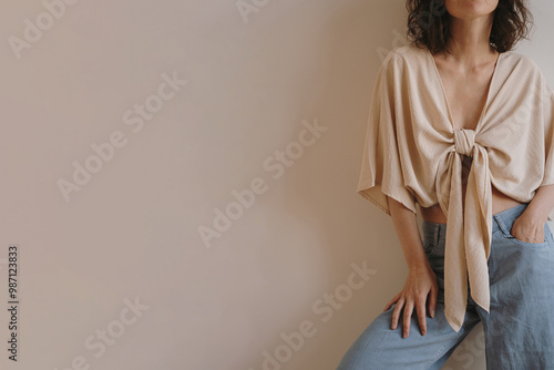 Woman in Chic Beige Tie-Front Top and Jeans. Fashionable Relaxed Style Indoor Portrait for Trendsetting Apparel Idea