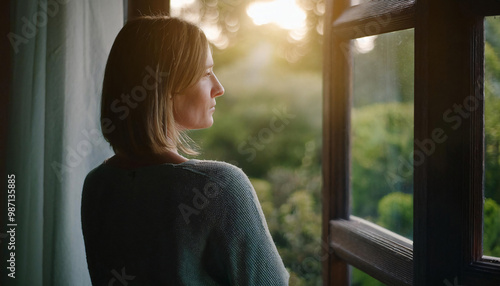 Young woman looking thoughtfully through the window into the garden.  photo