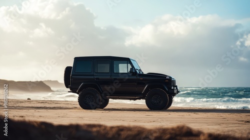 A black SUV parked on a sandy beach with waves crashing in the background, under a cloudy sky. photo