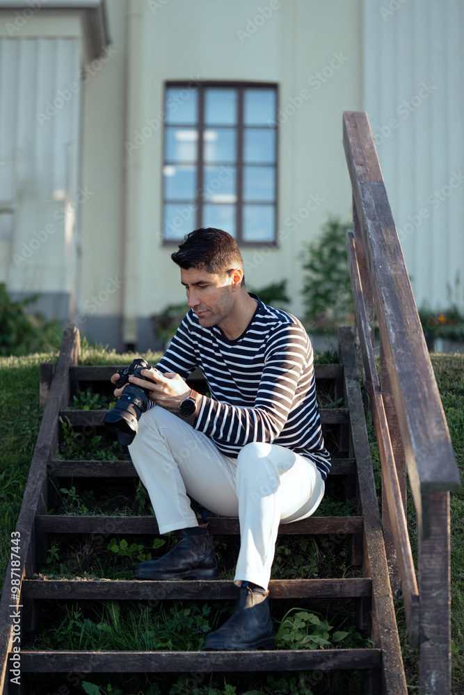 Obraz premium A young male photographer is sitting in front of a house, looking at the camera.