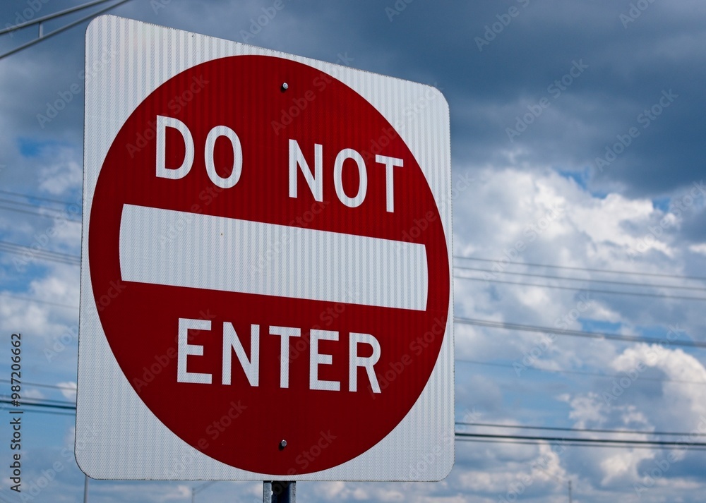 A red and white Do Not Enter sign on a cloudy background, with powerlines A red and white Do Not Enter sign on a cloudy background, with powerlines