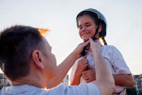 A father assists his young child with safety gear before an outdoor biking adventure. The image highlights wellness, fitness, and the importance of family support and preventive care for well-being.
