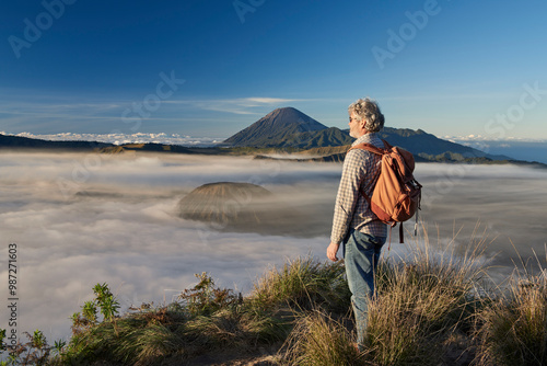 Asia, Indonesia, Java, Bromo Semeru national park, mature male tourist trekking at mount Bromo at sunrise, standing at viewpoint admiring view

 photo