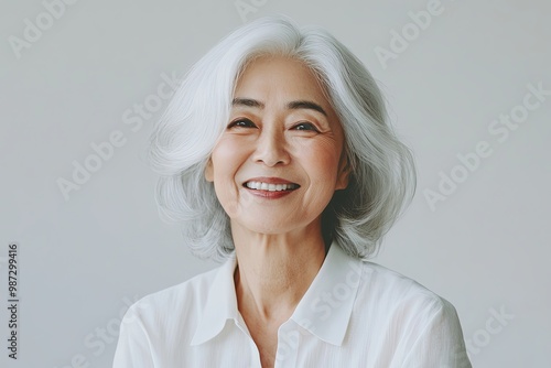 Smiling older Asian woman with silver hair, exuding warmth and joy against a soft, neutral background.