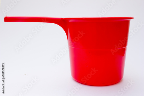 A red plastic dipper. This tool is used to collect water from the water storage tub.