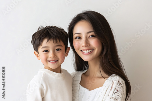 Young Japanese mother holding her cute young son, both looking into the camera, in front of a white studio background, showcasing a tender moment of family bonding and love