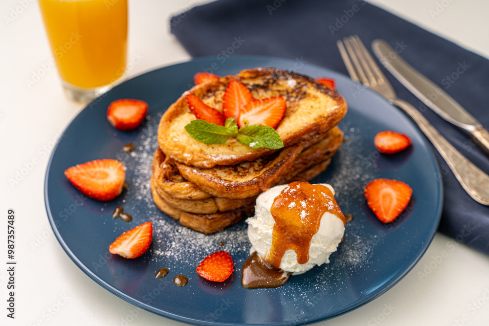French toast decorated with strawberries and mint leaves with ice cream drizzled with caramel sauce and powdered sugar on a blue plate and a glass of orange juice on a white background, table French toast decorated with strawberries and mint leaves with ice cream drizzled with caramel sauce and powdered sugar on a blue plate and a glass of orange juice on a white background, table