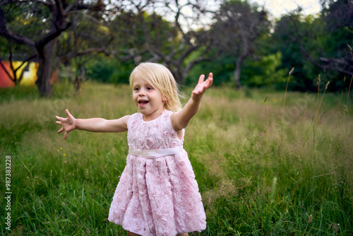 a toddler in a pink cloud of a dress runs like an airplane in the garden