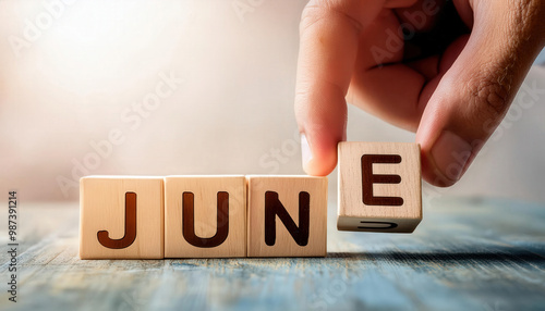 A hand is holding wooden blocks that spell out the word June