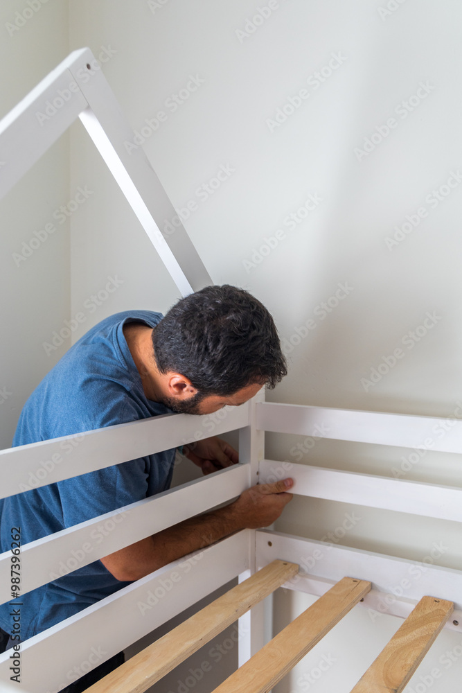 A man is working on a bed frame, possibly fixing it or building it A man is working on a bed frame, possibly fixing it or building it
