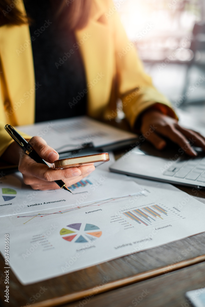Close-up of a business professional reviewing financial charts and graphs using a smartphone and laptop in a modern office environment. Close-up of a business professional reviewing financial charts and graphs using a smartphone and laptop in a modern office environment.