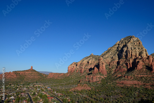 A breathtaking view of Sedona, Arizona, showcasing its iconic red rock formations set against a clear blue sky. The image captures a quiet residential area nestled among the dramatic desert landscape.