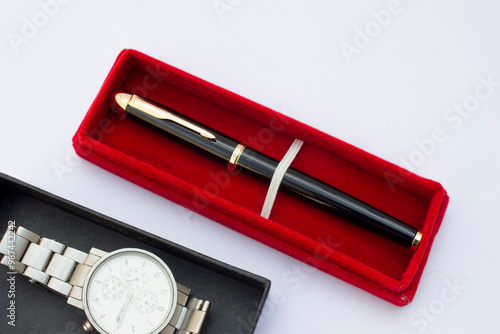 This image showcases a silver wristwatch alongside a ballpoint pen on a white background. The simple composition emphasizes the watch's design and the pen's everyday utility. photo