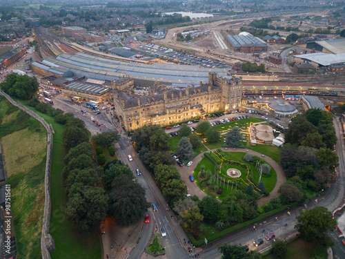Obraz na płótnie Beautiful illuminated York Railway Station and Principal York Hotel exterior at dusk. Aerial view of historic buildings and old city wall. Green park with trees and flag poles. Road with traffic. w salonie