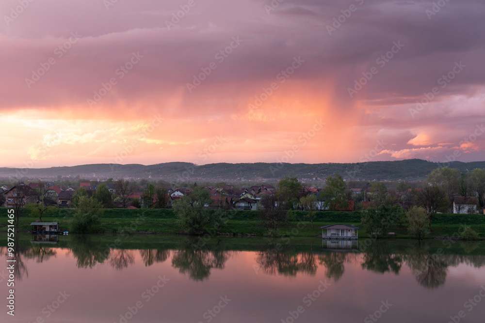 Strong downpour over hill behind settlement, sunlit clouds during sunset Strong downpour over hill behind settlement, sunlit clouds during sunset