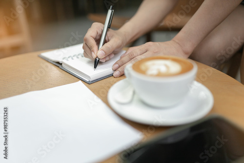 Women used a pen writing on the notebook on the table in the coffee shop. Selective focus and blurred background.