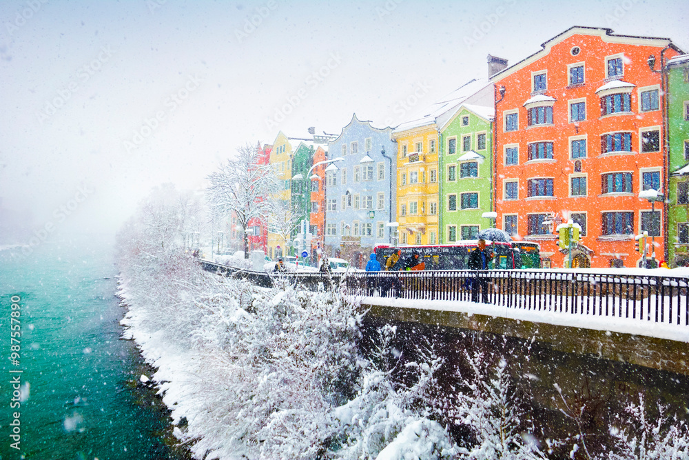 Obraz premium Snowy weather, colorful city houses, naked trees covered with snow and few people walk alongside the Inn river in Innsbruck, Tyrol (Tirol), western Austria, Europe