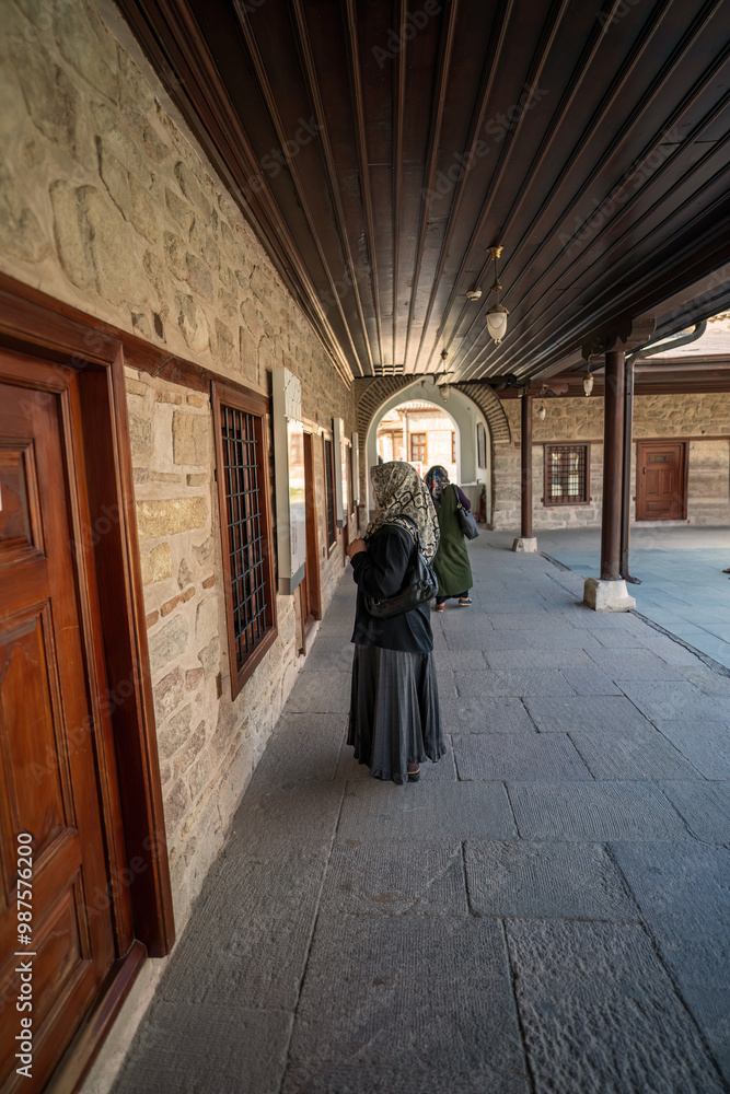Konya, Turkey: Women wearing a hijab and mask stands by a window, observing the traditional stone architecture of a historical building, Selimiye mosque in konya