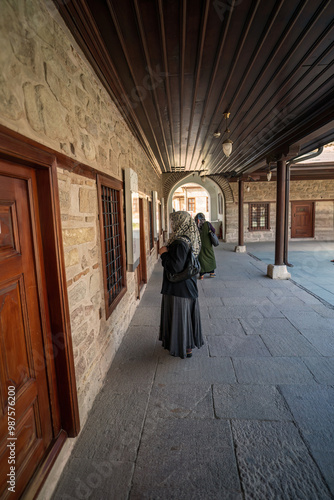 Obraz na płótnie Konya, Turkey: Women wearing a hijab and mask stands by a window, observing the traditional stone architecture of a historical building, Selimiye mosque in konya w salonie