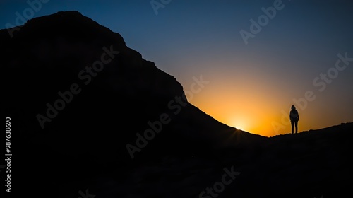 Silhouetted figure standing in the shadows as a majestic mountain landscape fades into the twilight of an atmospheric sunset evoking a sense of farewell and contemplation