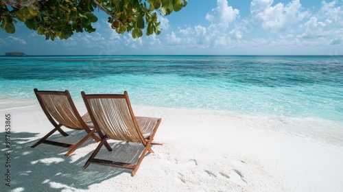 Two wooden lounge chairs facing the crystal-clear turquoise ocean under the shade of leafy trees on a pristine white sandy beach, perfect for a peaceful coastal escape. photo