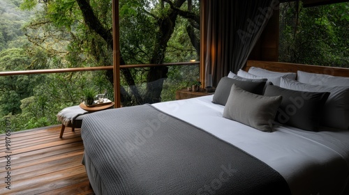 A serene bedroom featuring a comfortable bed with gray bedding, surrounded by large windows offering a stunning view of lush green forest, creating a peaceful retreat atmosphere. photo