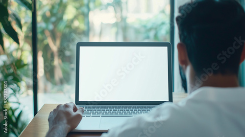 over-the-shoulder view of an Indian adult male student participating in an online meeting, with a blank white laptop screen prominently displayed, emphasizing the focus on virtual